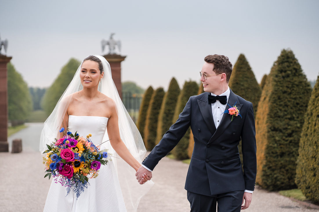 Bride and groom walking hand in hand through manicured gardens